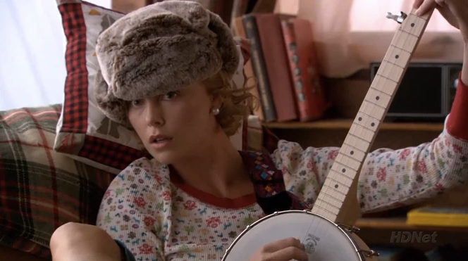 A young white woman is sitting and holding a banjo.
