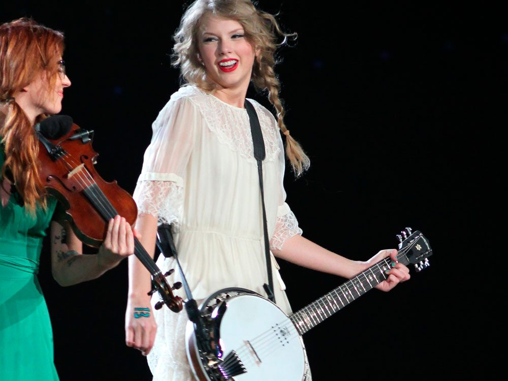 Taylor Swift, a young white woman, photographed onstage with her banjo.