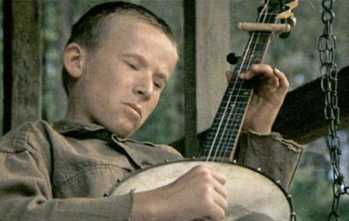 A young white boy is focusing intensely on his banjo while sitting.