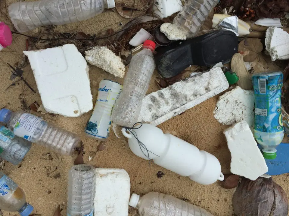 Trash on the beach to include pieces of styrofoam, a shoe, and plastic bottles.